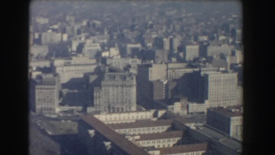 1960 Washington, DC aerial view with a broad cityscape, large rooftops, taller buildings, and hazy distance on vintage 8mm film.