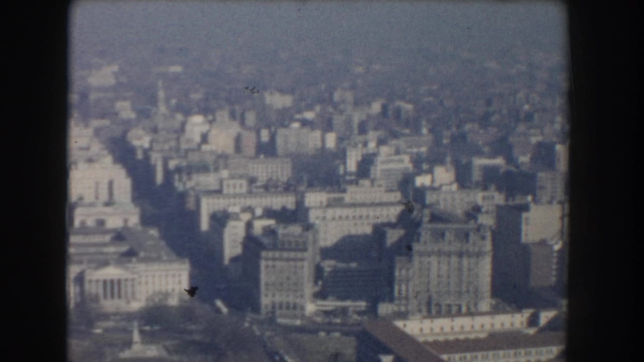1960 Washington, DC aerial frame with broad avenues, large civic buildings, urban blocks, and soft atmospheric haze.