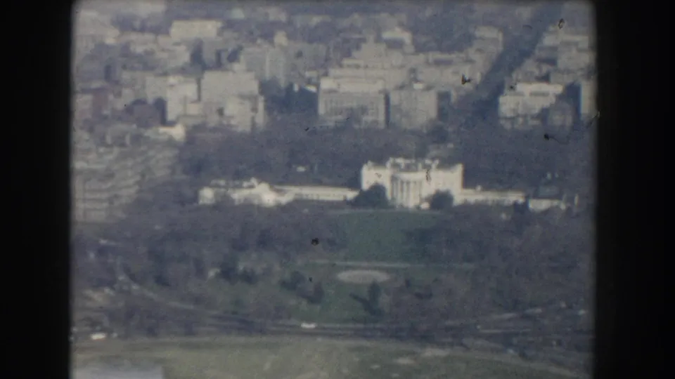 1960 Washington, DC aerial frame showing a large white civic building near open lawn, trees, and possible riverside parkland.