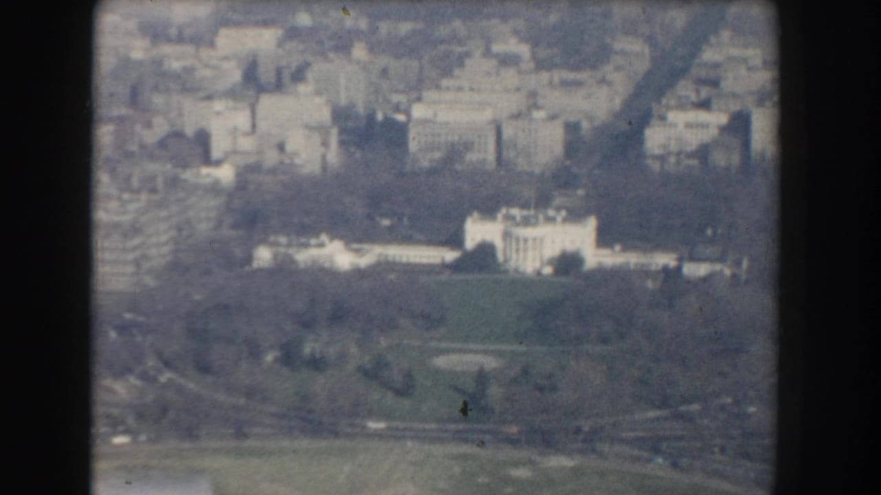 Aerial view of the White House, lawns, trees, and surrounding city buildings.