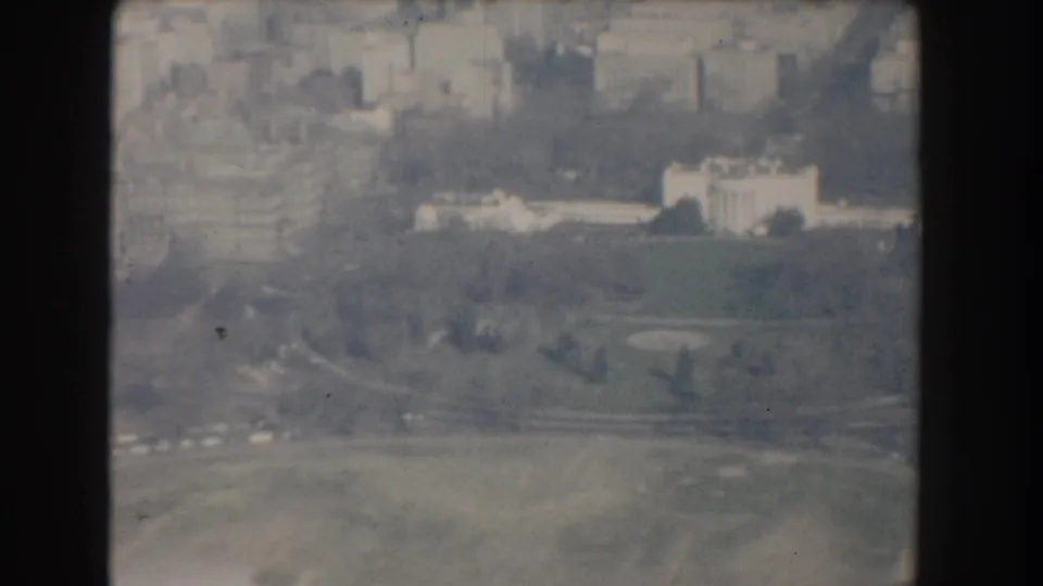 1960 Washington, DC aerial frame showing broad grounds, curving roads, trees, and distant institutional buildings in soft faded color.