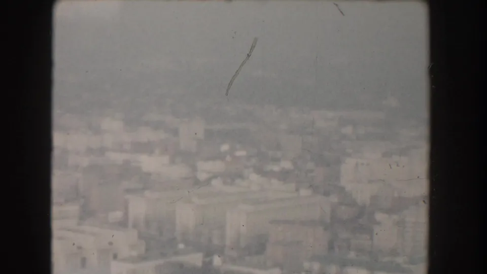 1960 Washington, DC aerial frame with blurred rooftops, streets, and pale structures softened by haze and 8mm film wear.
