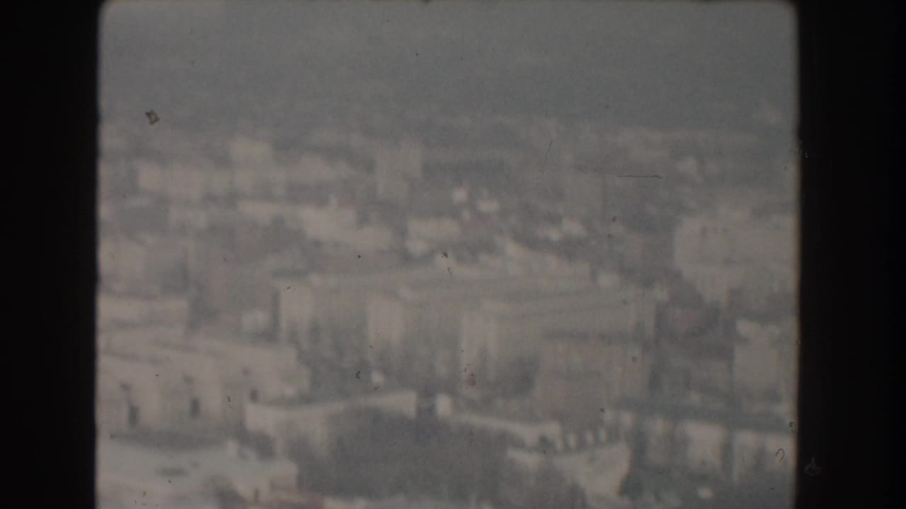 Soft aerial view over Washington, D.C. buildings seen through dark film-frame edges.