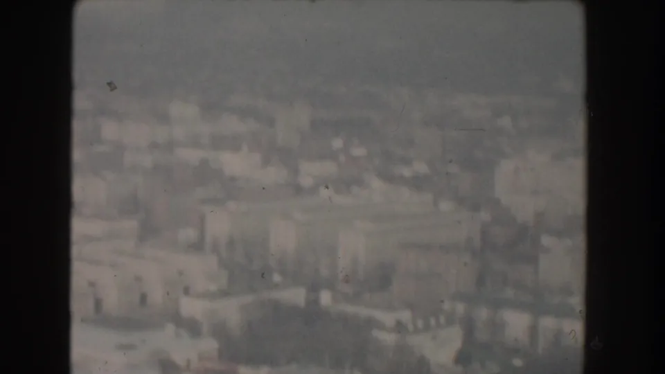 1960 Washington, D.C. aerial frame with hazy civic buildings and urban blocks visible through 8mm gate edges.