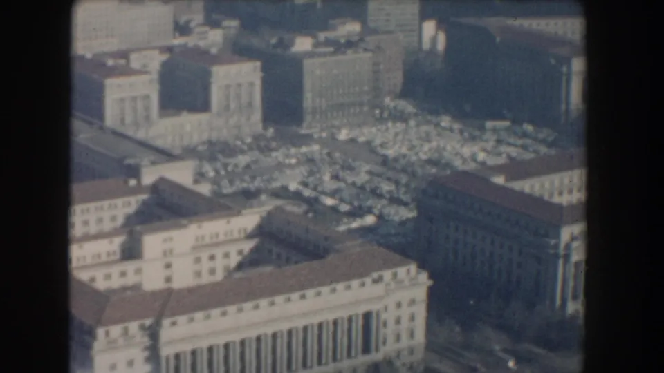 1960 Washington, DC aerial view with monumental civic buildings, rooflines, parked cars, and surrounding streets in soft 8mm haze.