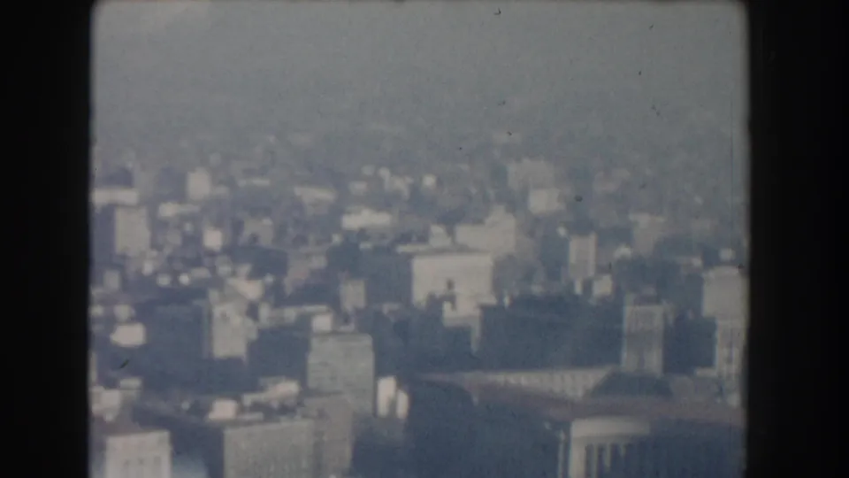 Hazy 1960 Washington, DC aerial city view with dense blocks, pale rooftops, and a large rounded roof form seen through soft focus.