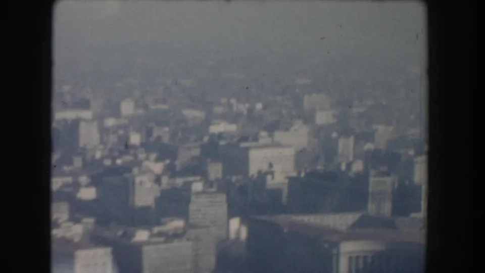 1960 Washington, DC aerial frame with soft, blurred city blocks, rooftops, and broad haze obscuring fine architectural detail.
