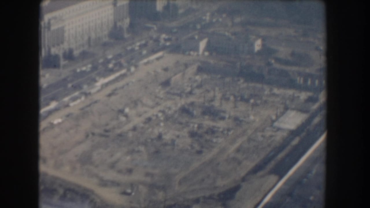 Aerial view of a large cleared construction site beside city streets and buildings.