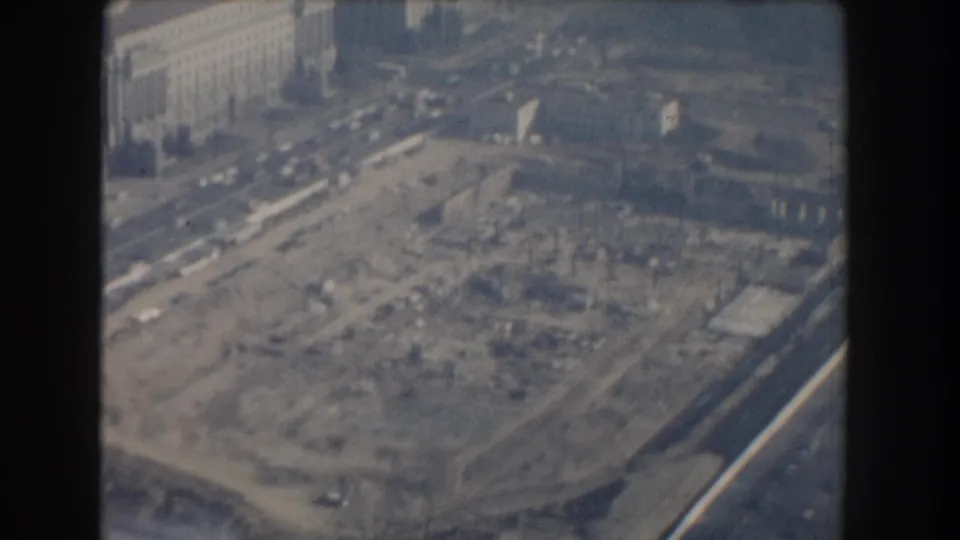 1960 Washington, DC aerial 8mm frame showing a construction site, nearby traffic, and large urban buildings through a hazy film image.