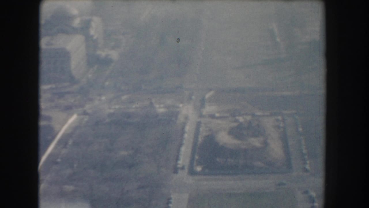 Hazy aerial view of streets, buildings, and a rectangular landscaped area.