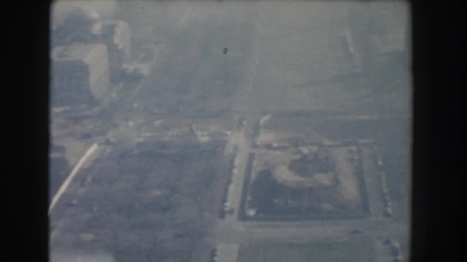 1960 Washington, DC aerial frame with hazy city blocks, traffic routes, and a rectangular open area near large buildings.
