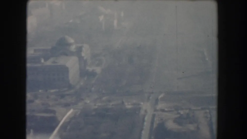 1960 Washington, DC aerial frame with large civic-looking buildings, nearby streets, and open ground in a grainy 8mm view.