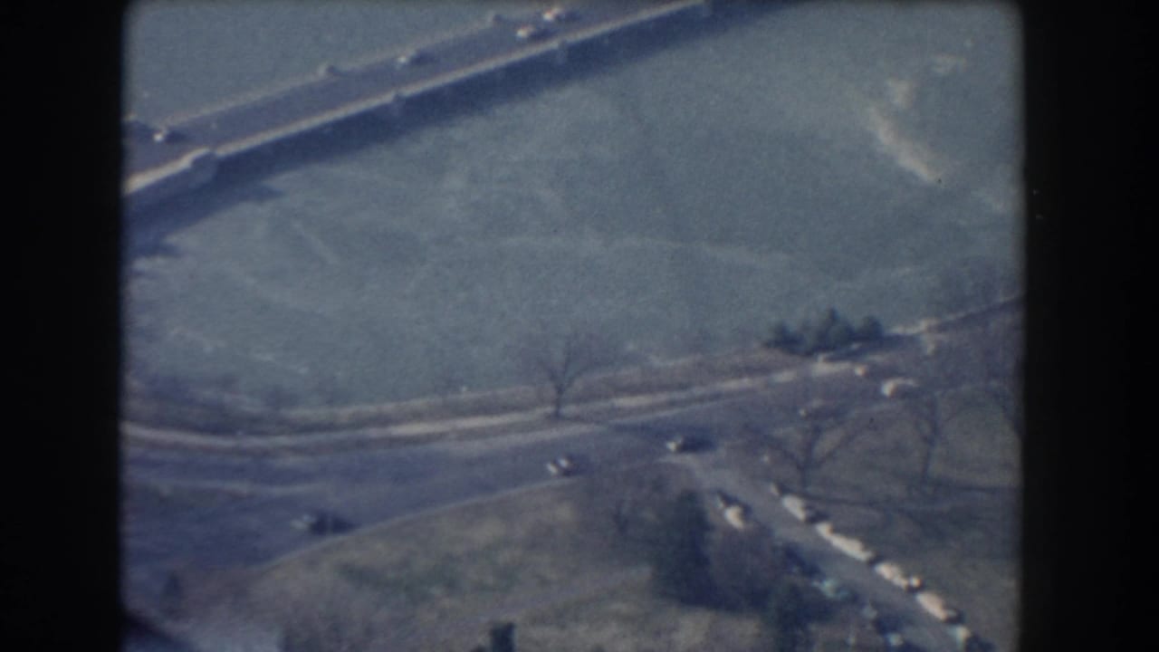 1960 Washington, DC aerial frame showing a long bridge over water with small cars moving along the roadway.