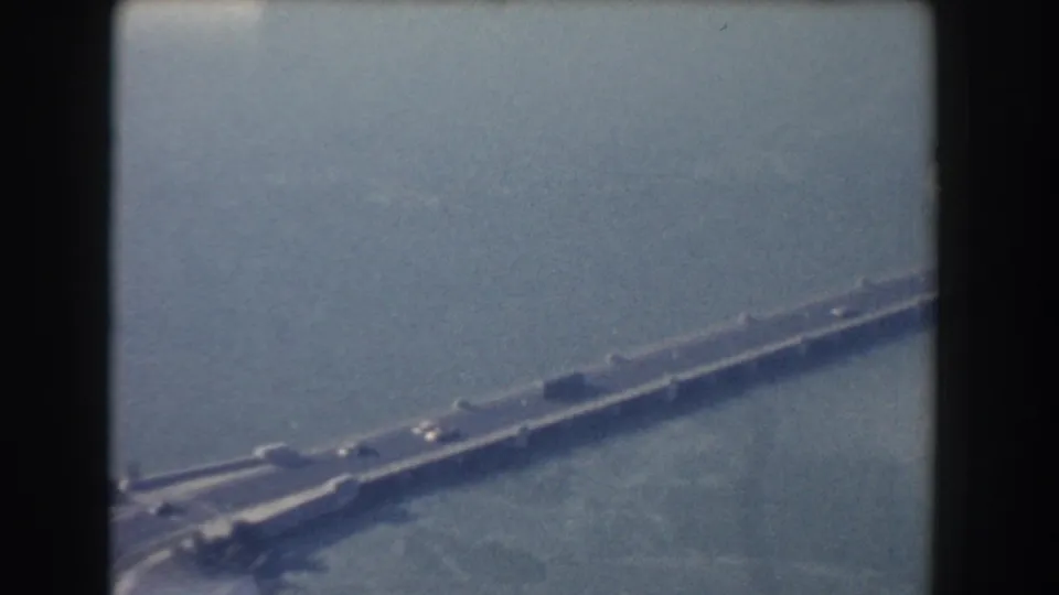 Blue-tinted 8mm frame of a Washington, DC bridge span over water, with traffic and a road approach visible below.