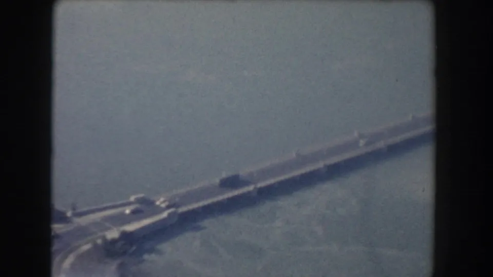 1960 Washington, DC home-movie frame showing a distant bridge over a broad river with light traffic and soft haze.