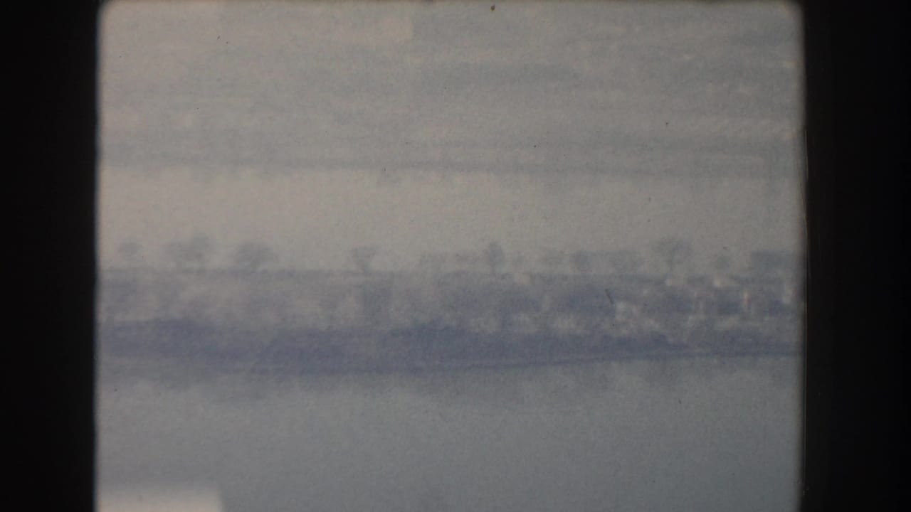 Hazy view across water with a distant shoreline and dark film border.