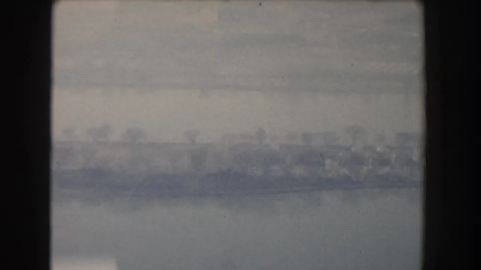 1960 archival home-movie frame showing hazy water, a faint shoreline, and possible bridge or urban edge in the Washington, DC area.