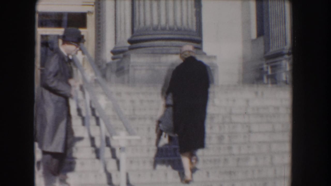 Two adults walk up stone museum steps beside railings and columns.