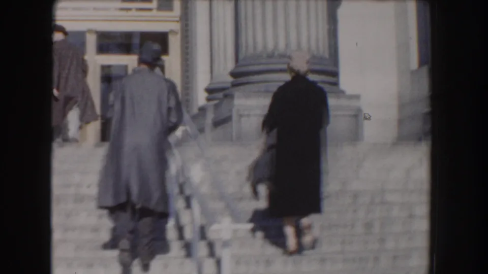 A man in a hat and a woman in a dark coat walk up the Smithsonian Natural History Building steps in Washington, DC.