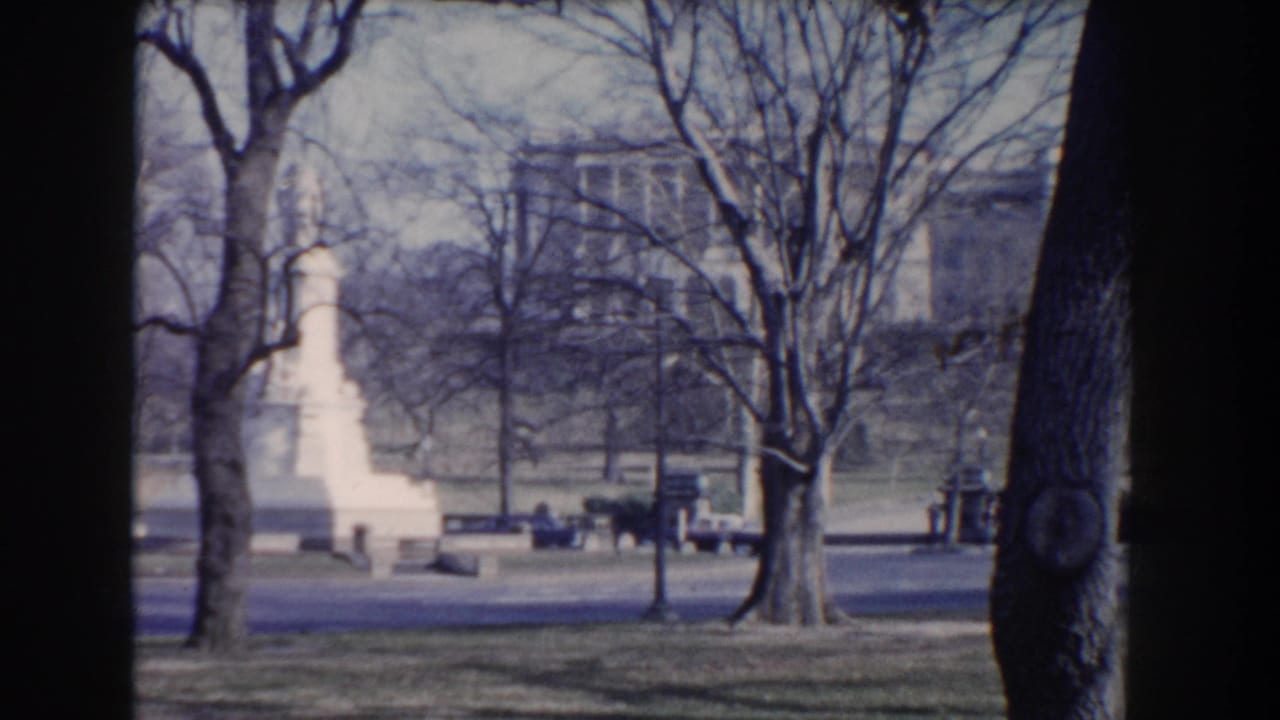 Visitor-shot 1960 Washington, DC view across a road toward a white monument, benches, bare trees, and civic buildings.