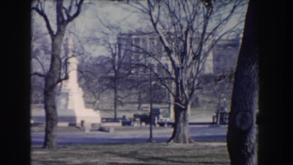Visitor-shot 1960 Washington, DC view across a road toward a white monument, benches, bare trees, and civic buildings.