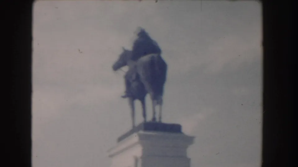 1960 Washington, DC home-movie frame showing a rider on horseback statue above a stone pedestal in soft focus.