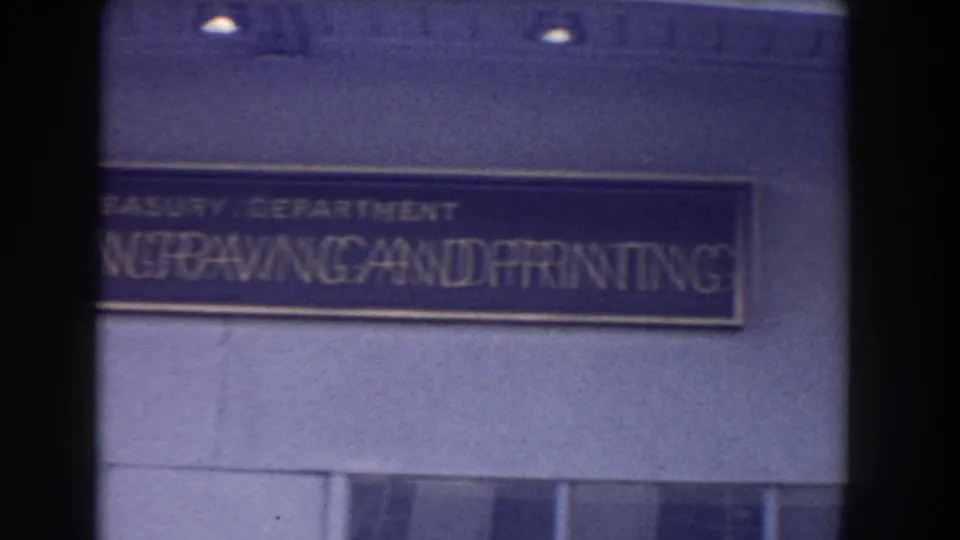 Home-movie frame of the Bureau of Engraving and Printing sign on a Washington, DC building facade in muted 8mm color.