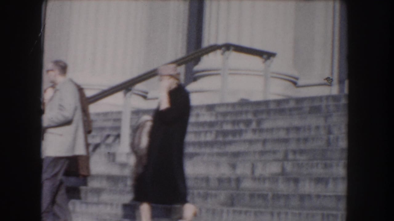 Two adults walking beside stone steps in front of a classical building.