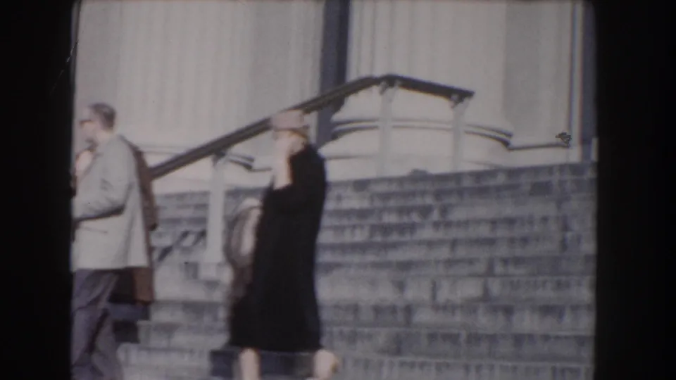 Circa-1960 Washington, DC home-movie frame showing two adults near broad stone steps and a classical facade.