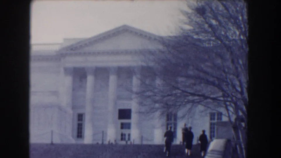1960 Washington, DC 8mm frame of a neoclassical public building with a pediment, columns, bare tree branches, and visitors near the steps.