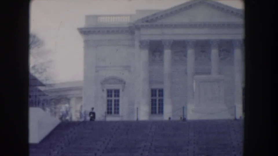 1960 Washington, DC 8mm frame showing the right side of a neoclassical facade, broad steps, tall windows, and small distant visitors.