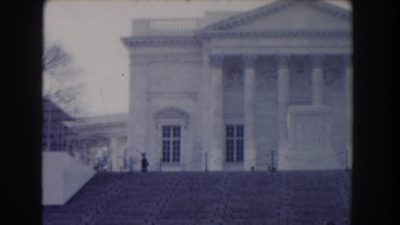 Distant view of a white neoclassical facade with columns, steps, and a small figure near the stairway.