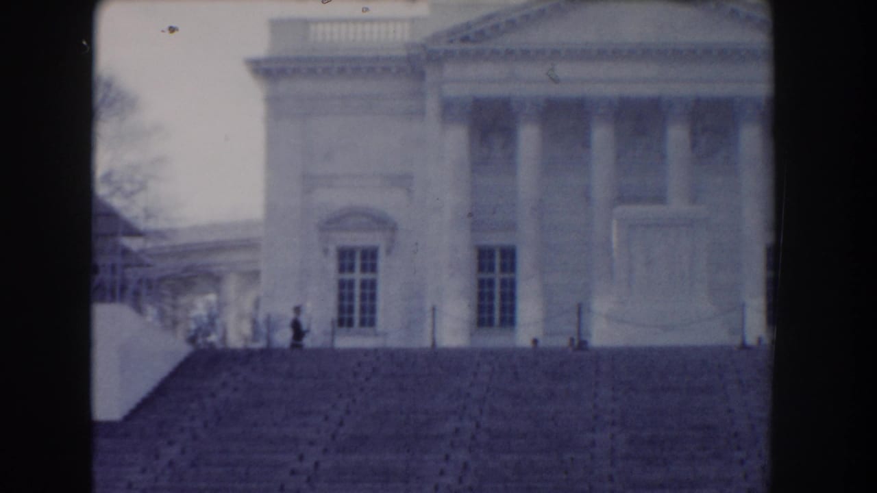 Similar distant view of the columned building and steps with a small person near the railing.
