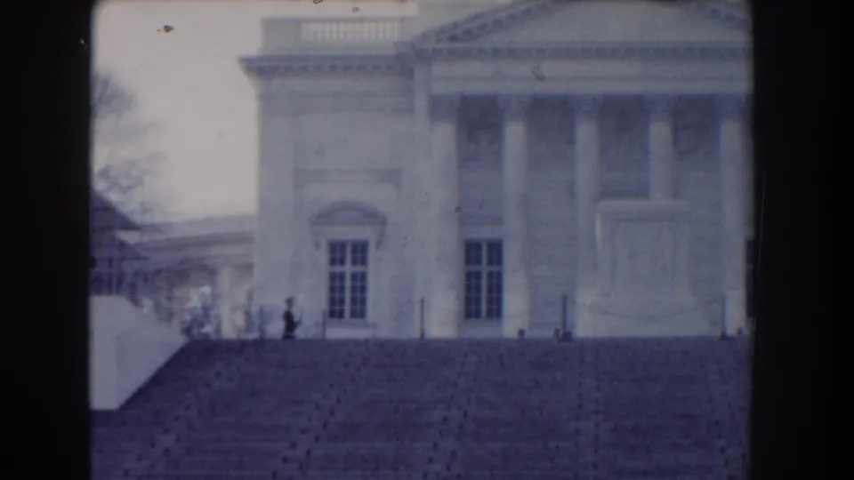 1960 Washington, DC frame with a columned civic facade, wide steps, windows, and a small visitor visible near the stair railing.