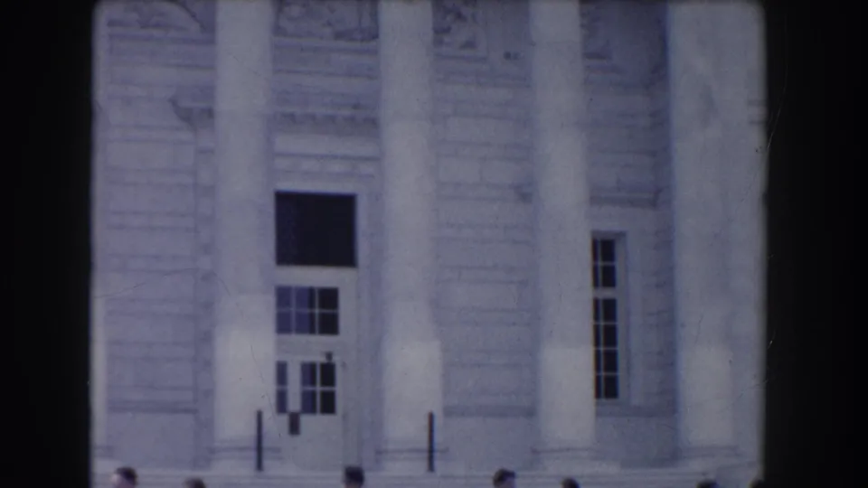 Close 1960 Washington, DC frame showing tall columns, carved facade detail, steps, railings, and visitors along the lower edge.