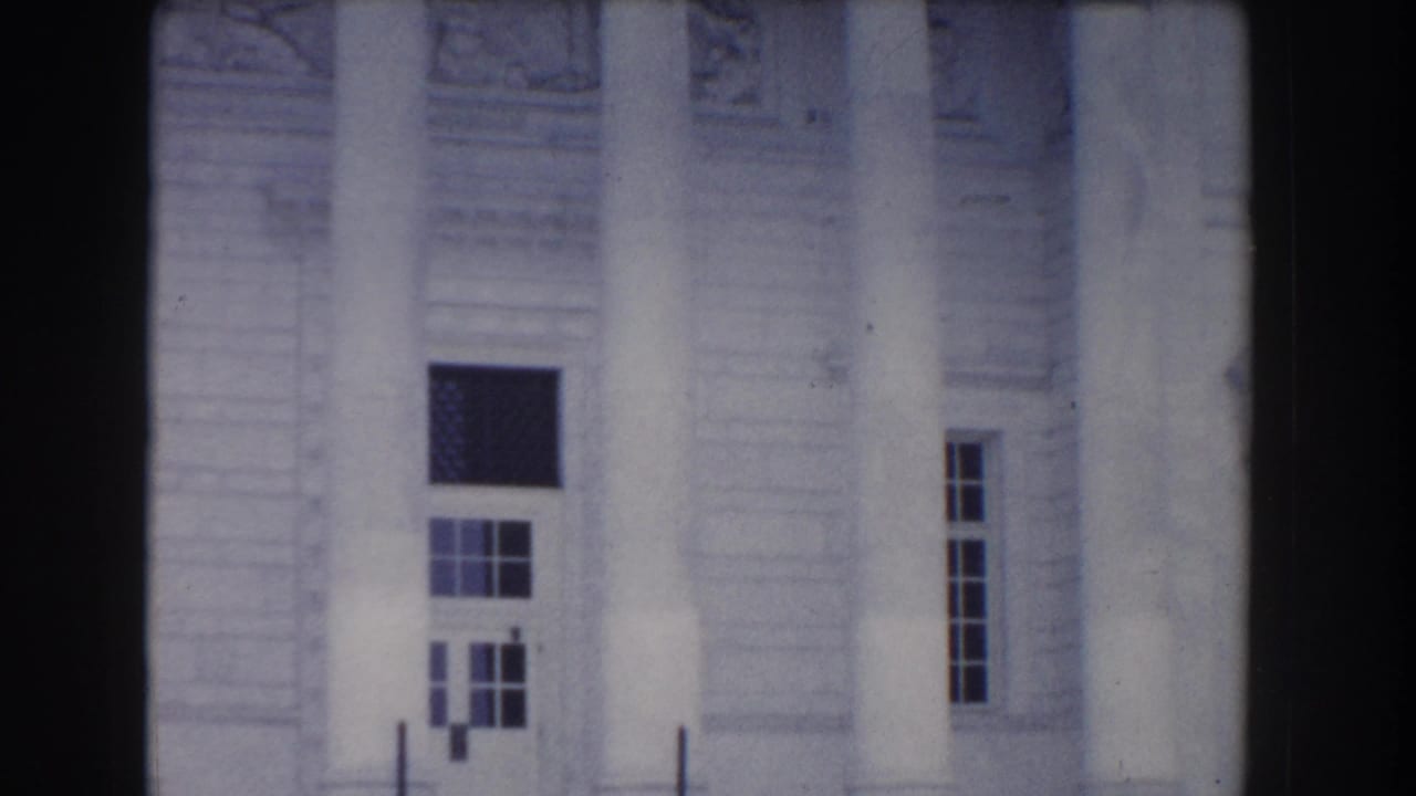 White stone building facade with columns and rectangular windows.