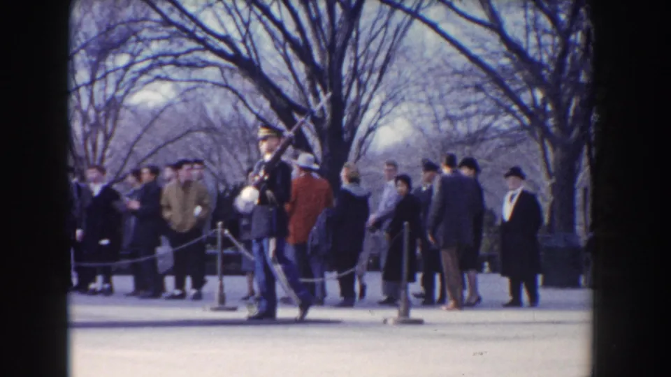 Washington, DC visitors in winter clothing watch as a formal guard with rifle moves along a roped walkway.