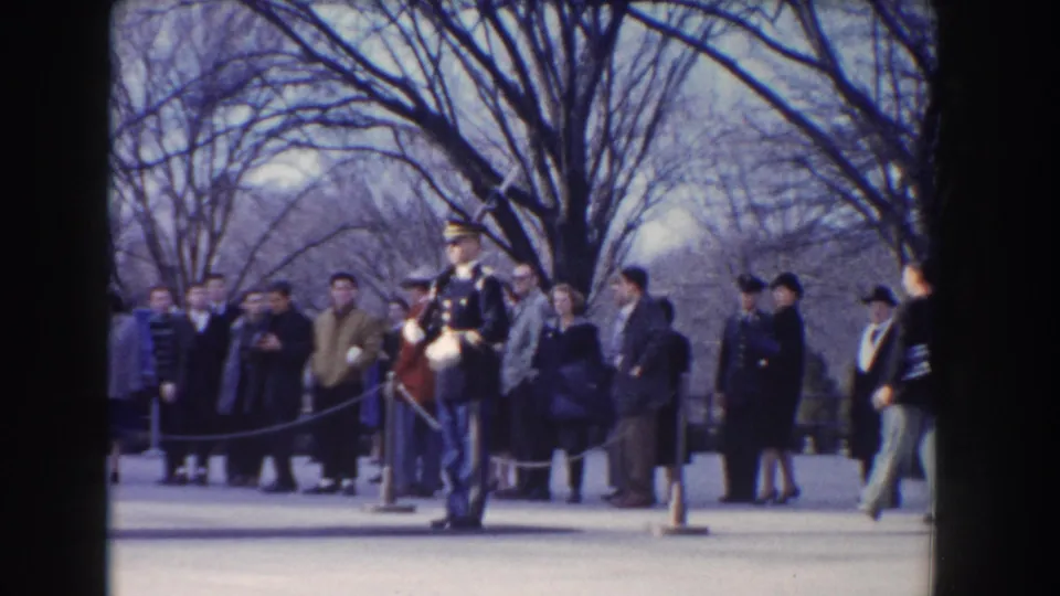1960 Washington, DC home-movie frame of a dress-uniform guard standing at attention while civilians watch from behind a rope line.