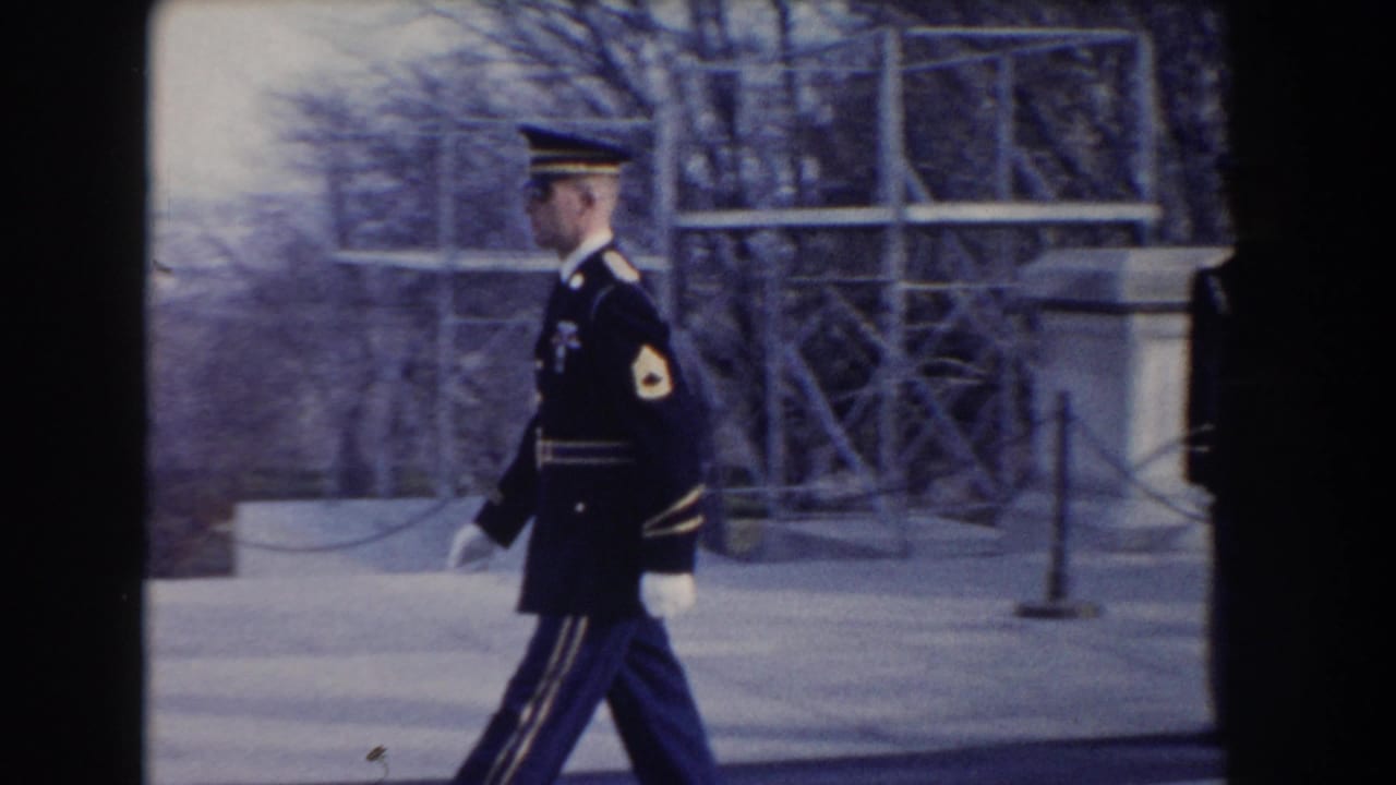 Uniformed guard walking past pale stone and chain barriers.