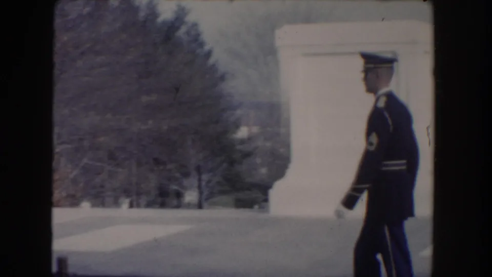 A uniformed guard crosses an open paved area near a white stone structure, filmed from a handheld visitor angle in Washington, DC.