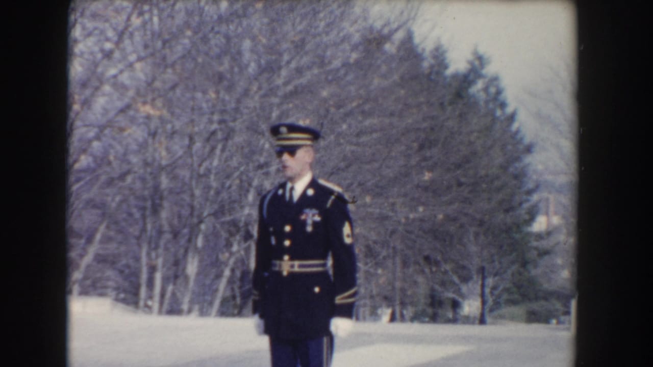 1960 Washington, DC frame of a ceremonial guard in dark uniform standing at attention against bare trees.