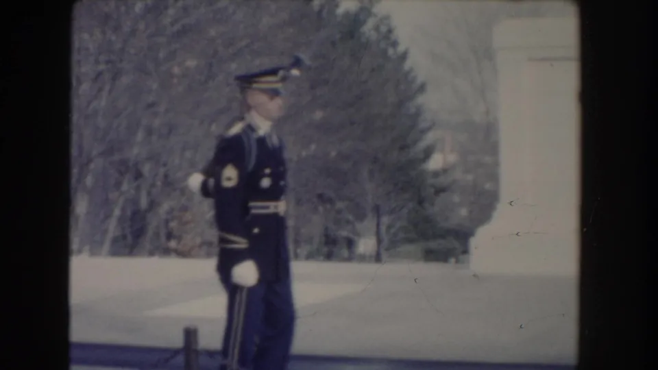 1960 Washington, DC home-movie frame showing a ceremonial guard marching outdoors beside a pale monument-like structure.