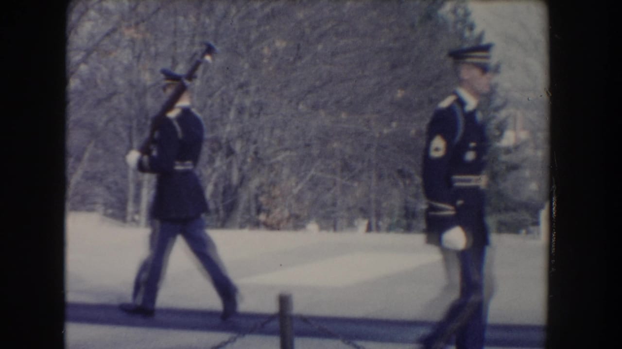 Two uniformed guards with rifles move across a paved outdoor area in winter light.