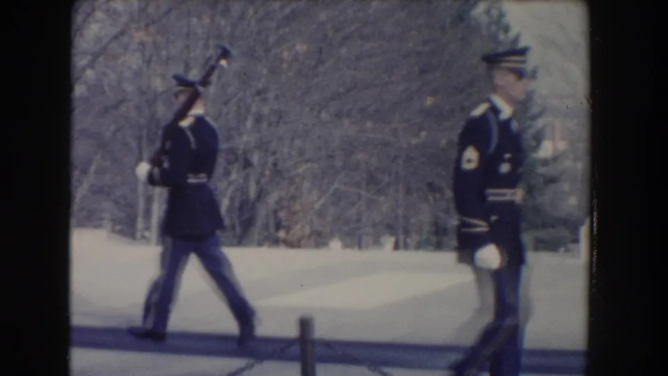 1960 Washington, DC home-movie frame showing uniformed military guards with ceremonial rifles near bare trees and a paved walkway.
