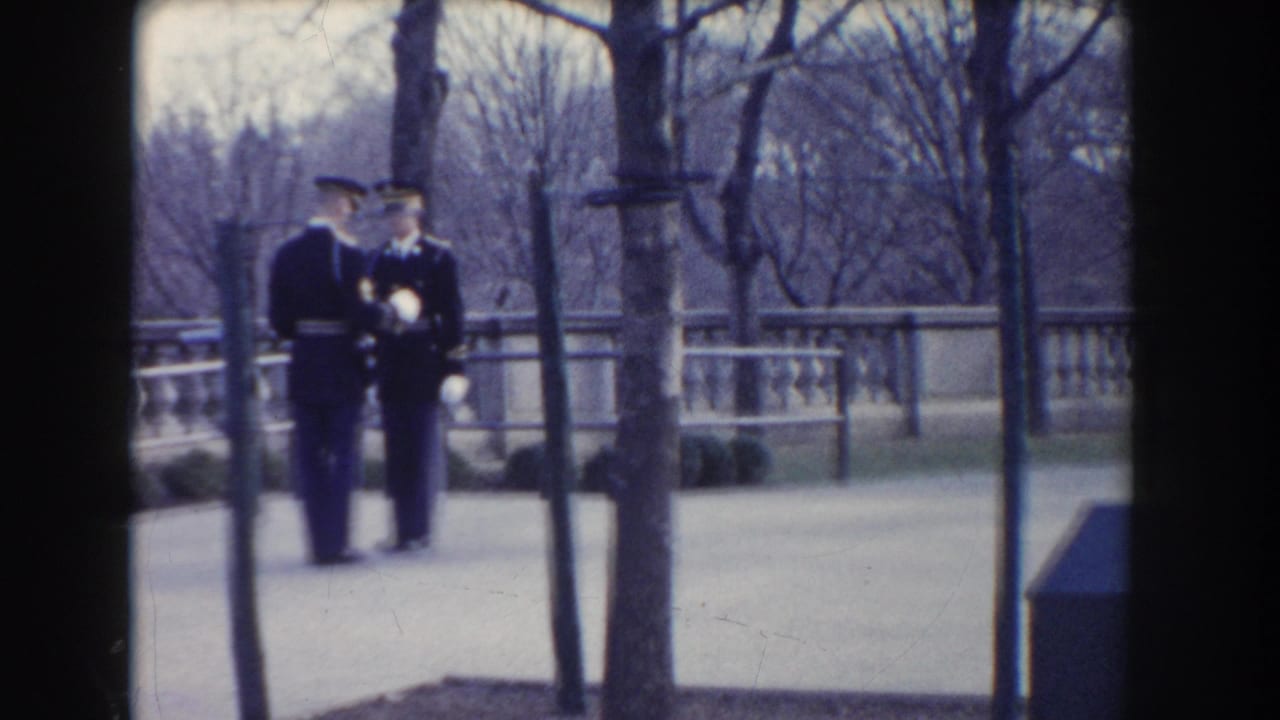 Two soldiers in dark uniforms stand close together on a walkway with trees and a balustrade behind them.
