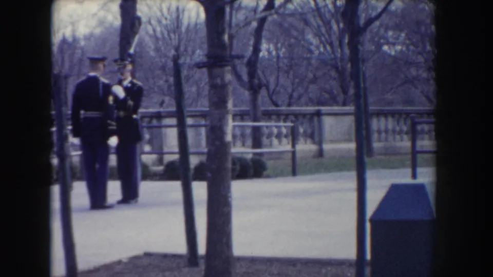 A 1960 Washington, DC 8mm frame shows two soldiers in dark uniforms standing with rifles near trees and a stone balustrade.