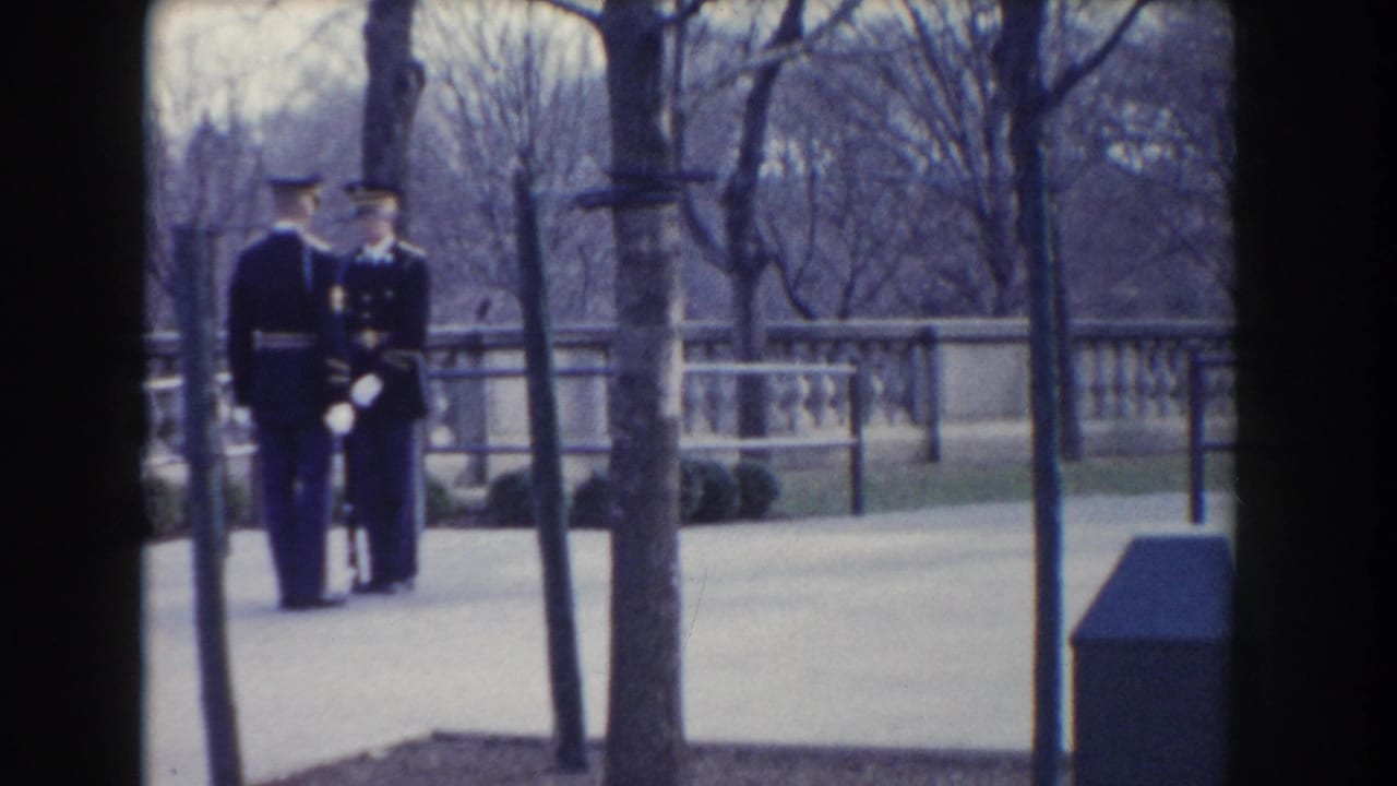 Two uniformed guards stand together on a paved walk near bare trees and a stone balustrade.