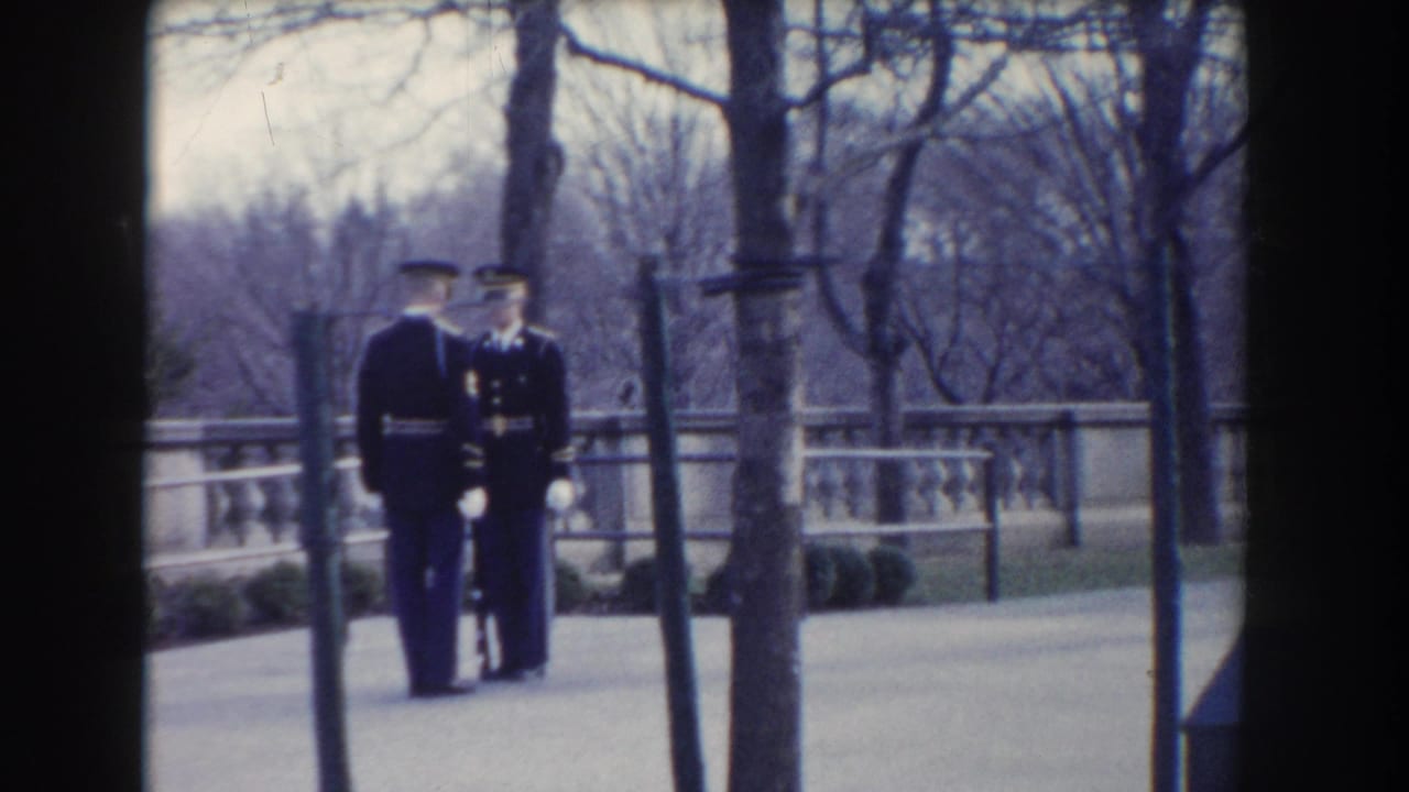 Two uniformed guards stand side by side near trees, railings, and a stone balustrade.