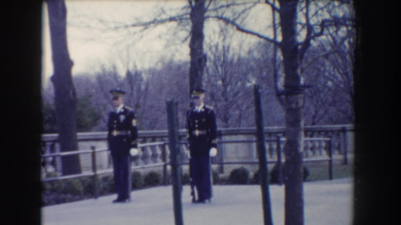 Two uniformed Marines stand outdoors near a stone balustrade and bare trees.