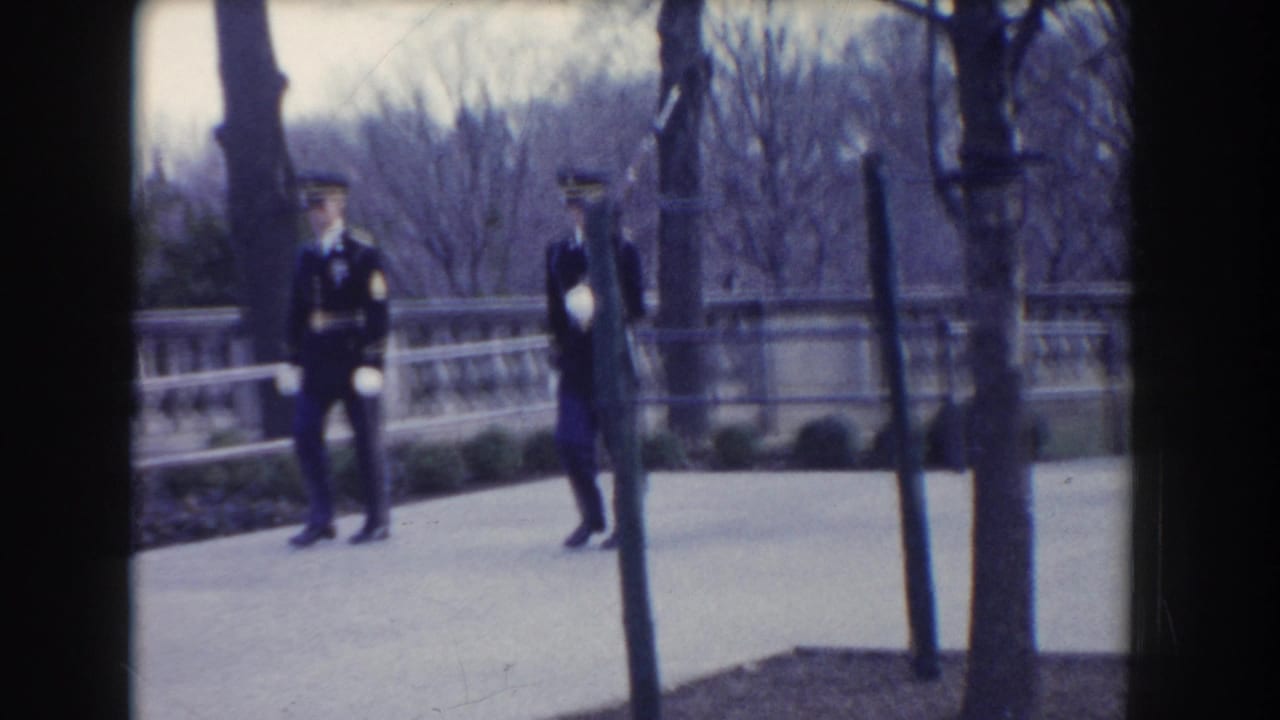 Two uniformed guards stand or move on a paved path near a stone balustrade and bare trees.